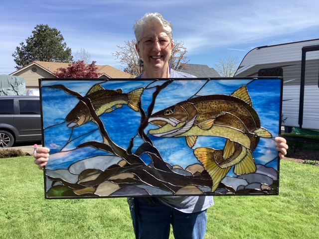 Maryann Birkel holding the completed brown trout stained glass panel.