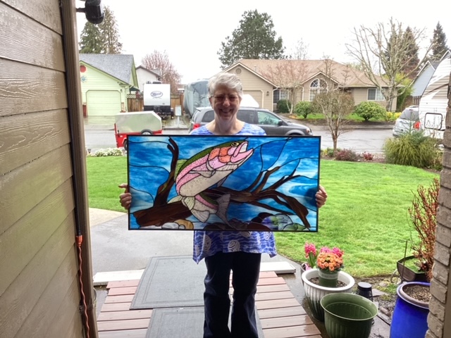 Maryann Birkel holding the completed rainbow trout stained glass panel.